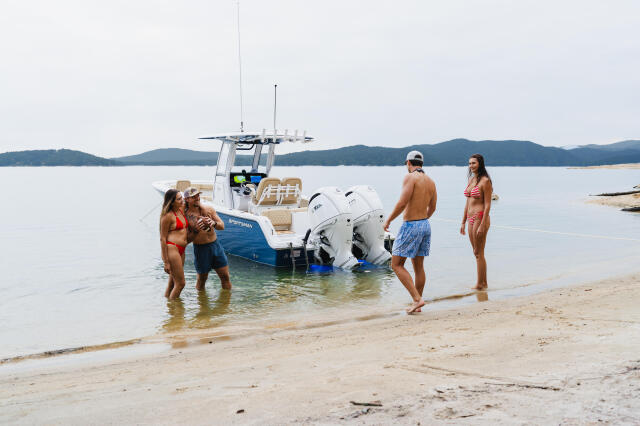 Group of friends swimming and relaxing at a beached center console boat on a sandbar with mountains in the distance