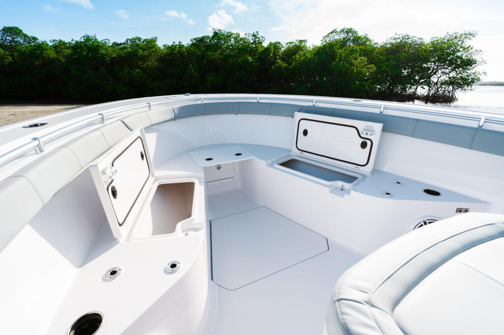 White center console boat cockpit with cushioned seating, storage compartments, and mangrove shoreline in background