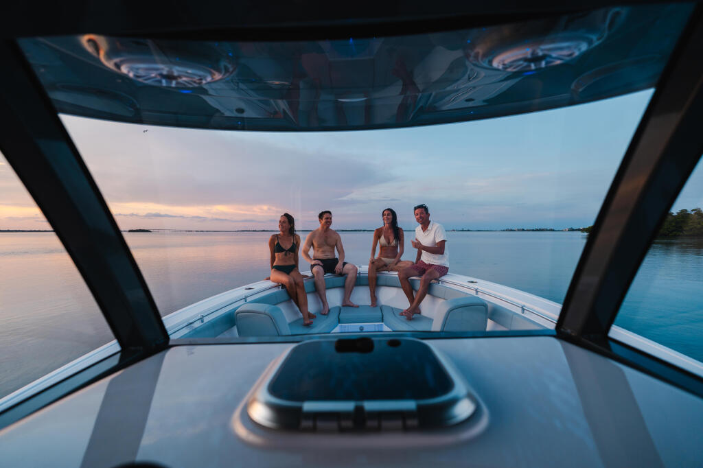 Four friends relaxing on the bow of a boat at sunset with calm water and sky in the background