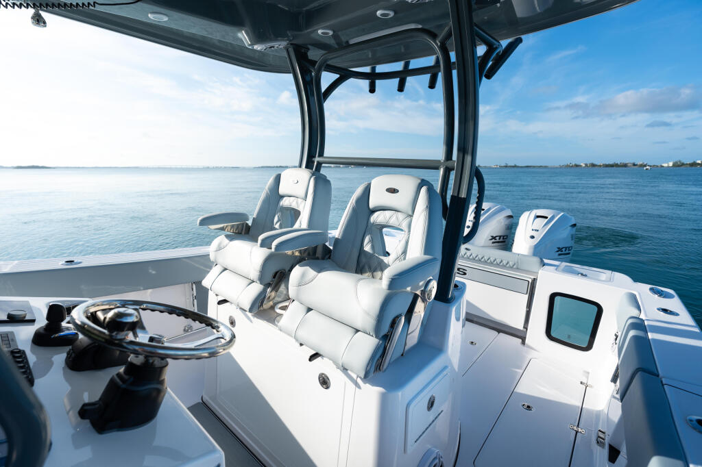Helm area of center console boat with steering wheel, padded seating, hard-top canopy, and calm blue water ahead