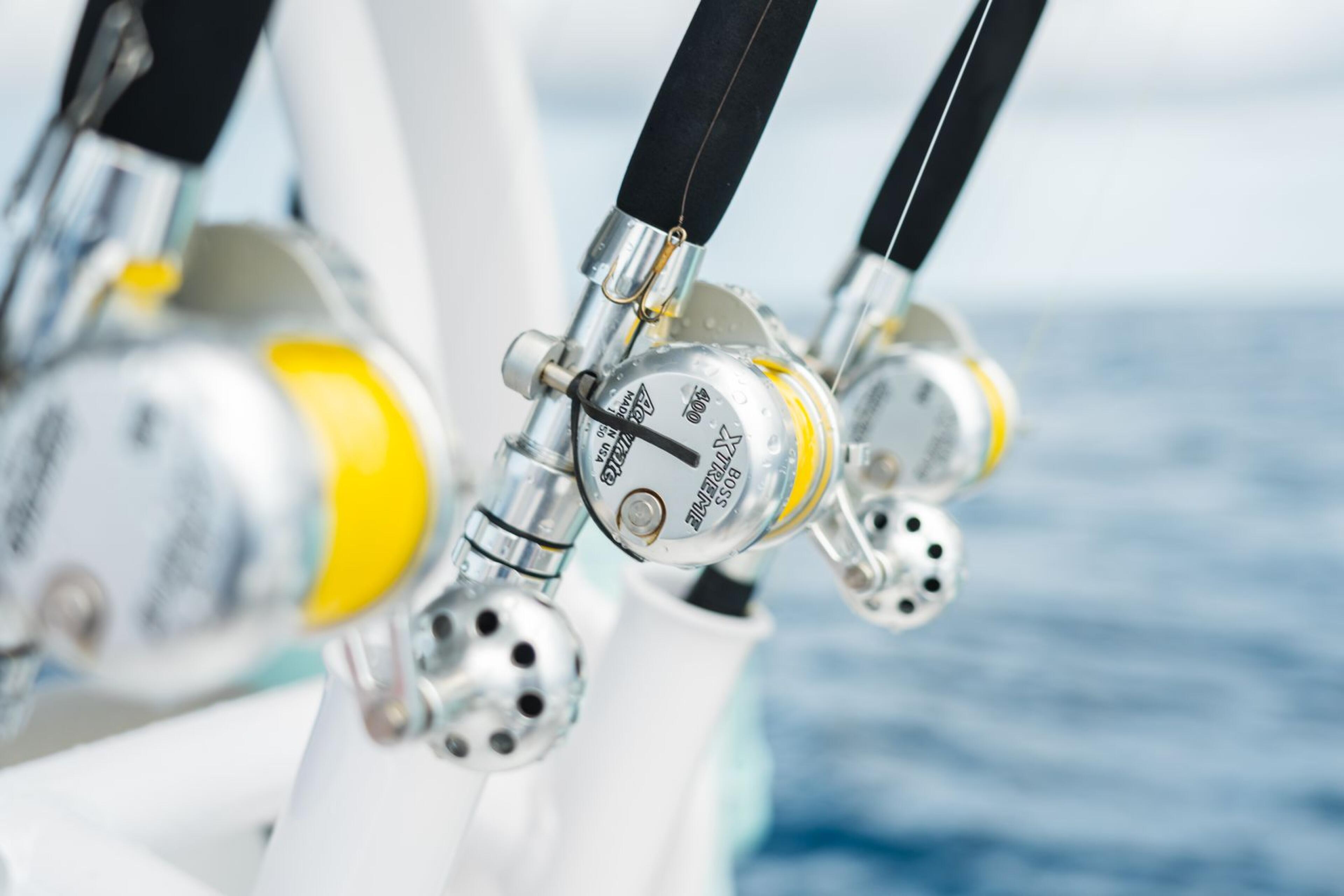 Multiple fishing reels with yellow and silver detailing mounted on a boat rail overlooking open ocean