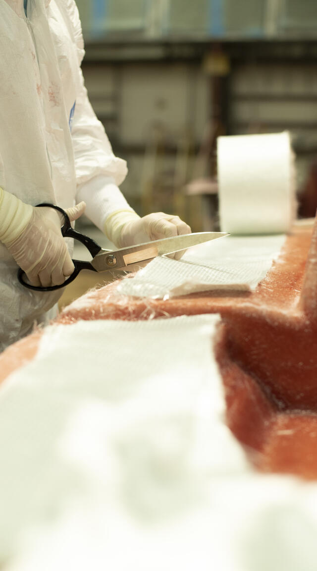 Person in white protective gear carefully cutting fiberglass or composite material with scissors