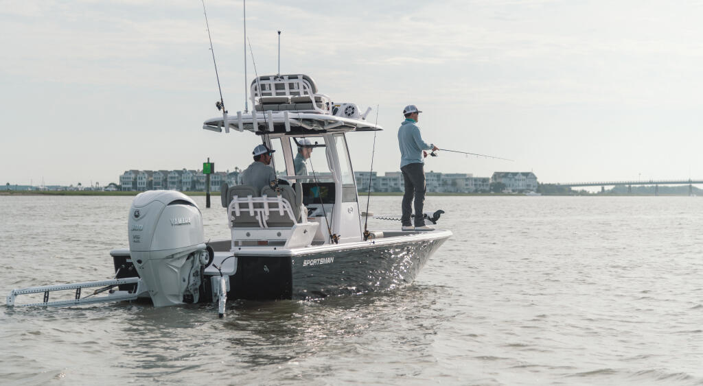 Two anglers fishing from a center console boat in shallow coastal waters near residential buildings