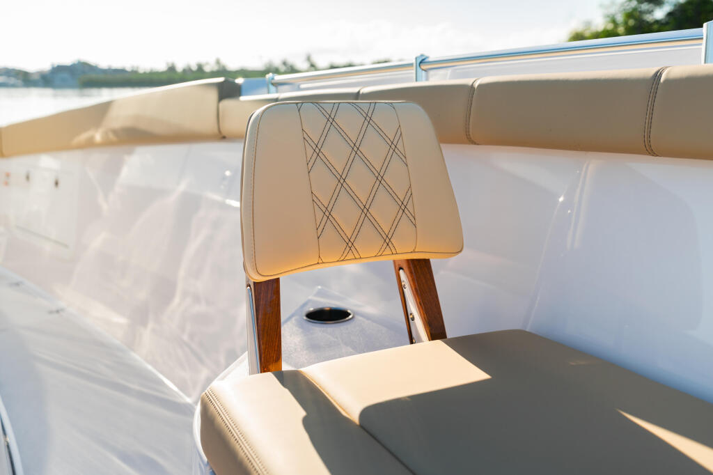 Cream-colored quilted captain's chair with wooden armrests on a sunlit boat deck overlooking calm water