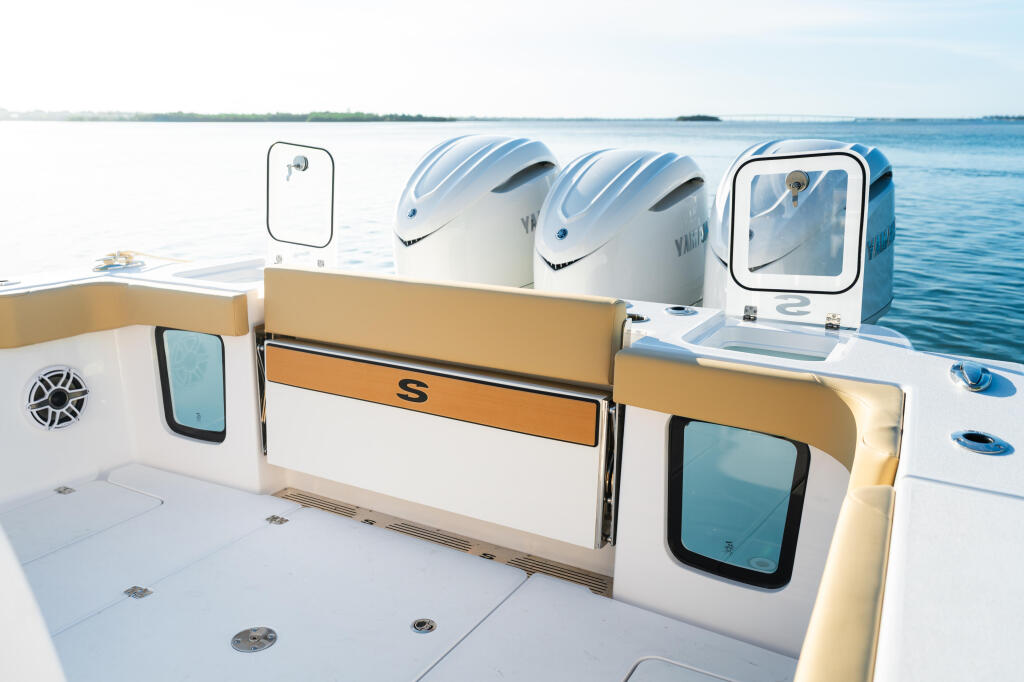 Spacious aft deck with twin outboard engines, cushioned seating, and storage compartments on a center console fishing boat