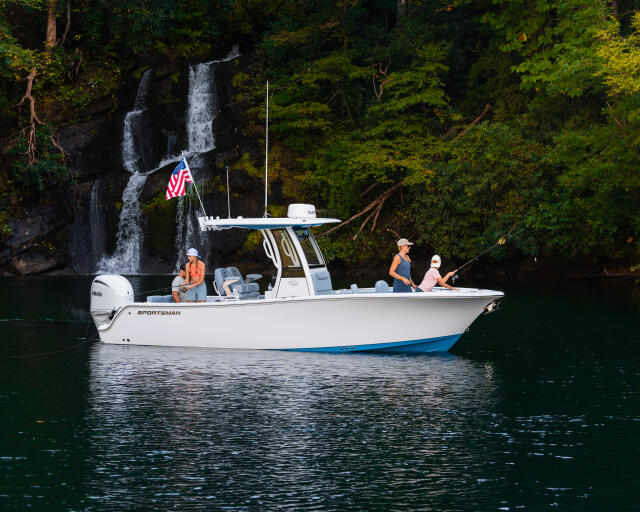 Sportsman center console boat anchored in clear water near a waterfall with anglers fishing and a US flag flying