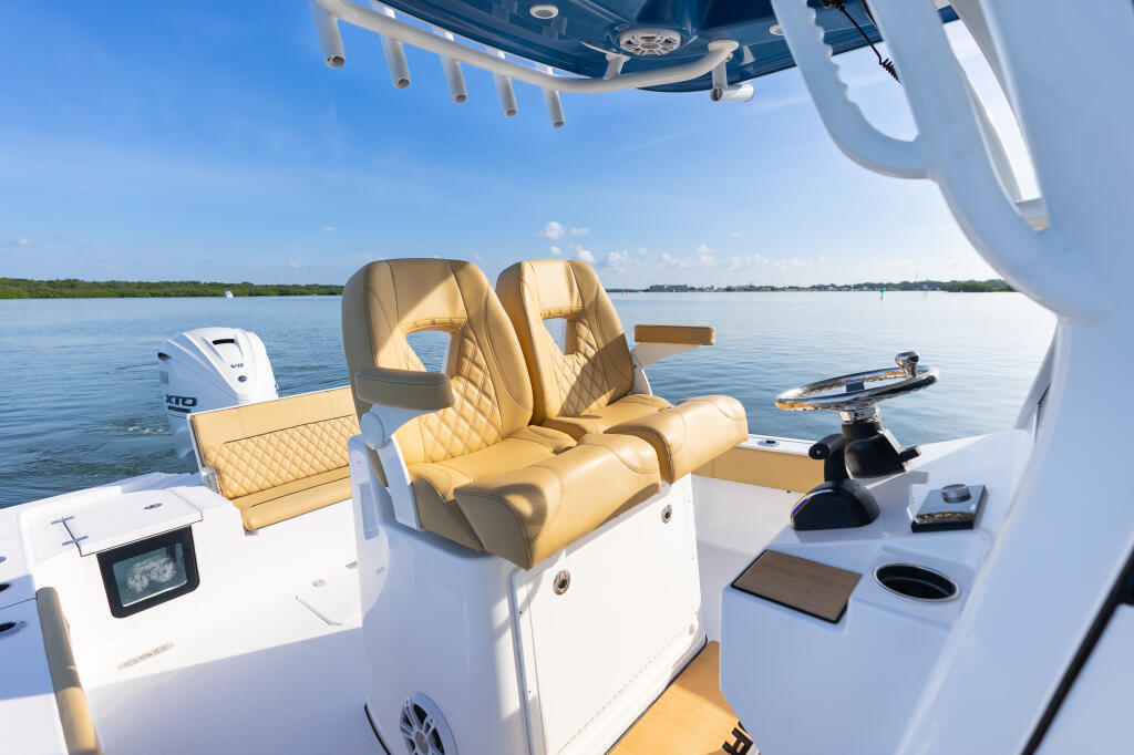 Helm view of center console boat with tan leather captain's chairs, hardtop, and calm water ahead