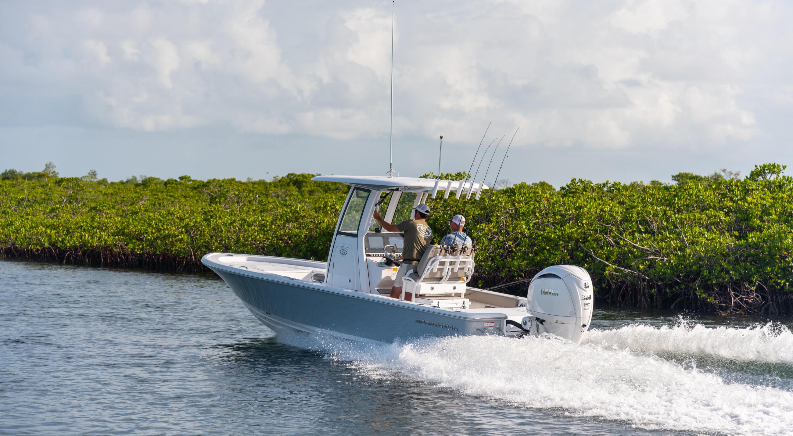 Fishing boat with anglers and multiple rod holders cruising through shallow mangrove waters