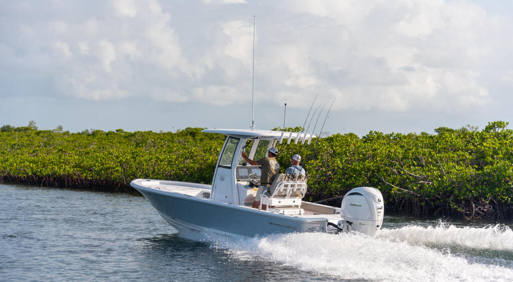 Fishing boat with anglers and multiple rod holders cruising through shallow mangrove waters