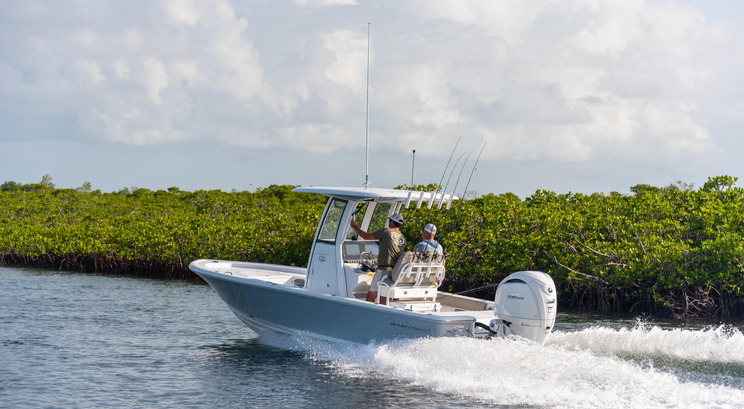 Fishing boat with anglers and multiple rod holders cruising through shallow mangrove waters