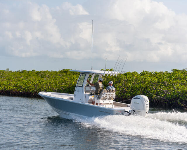 Fishing boat with anglers and multiple rod holders cruising through shallow mangrove waters