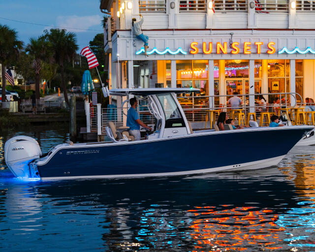 Blue and white center console boat docked at sunset restaurant marina with families dining