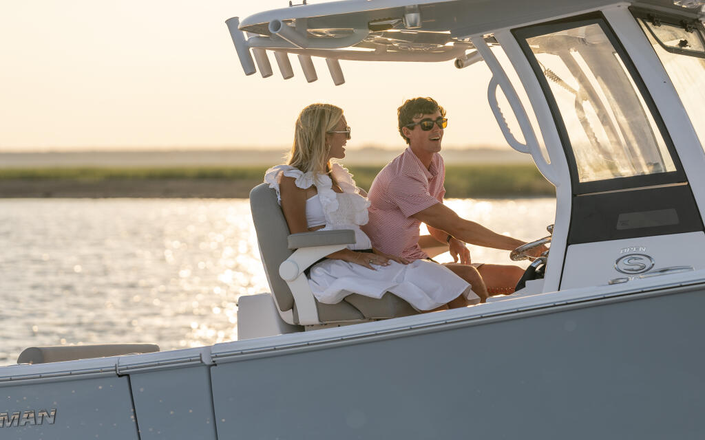 Couple at the helm of a center console boat during golden hour with calm water behind them