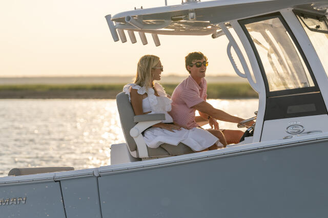 Couple at the helm of a center console boat during golden hour with calm water behind them