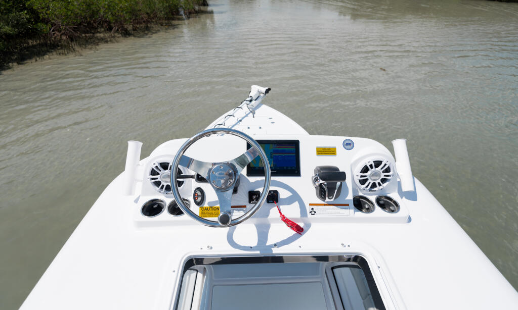 Overhead view of boat helm with steering wheel, electronics, speakers, and mangrove shoreline
