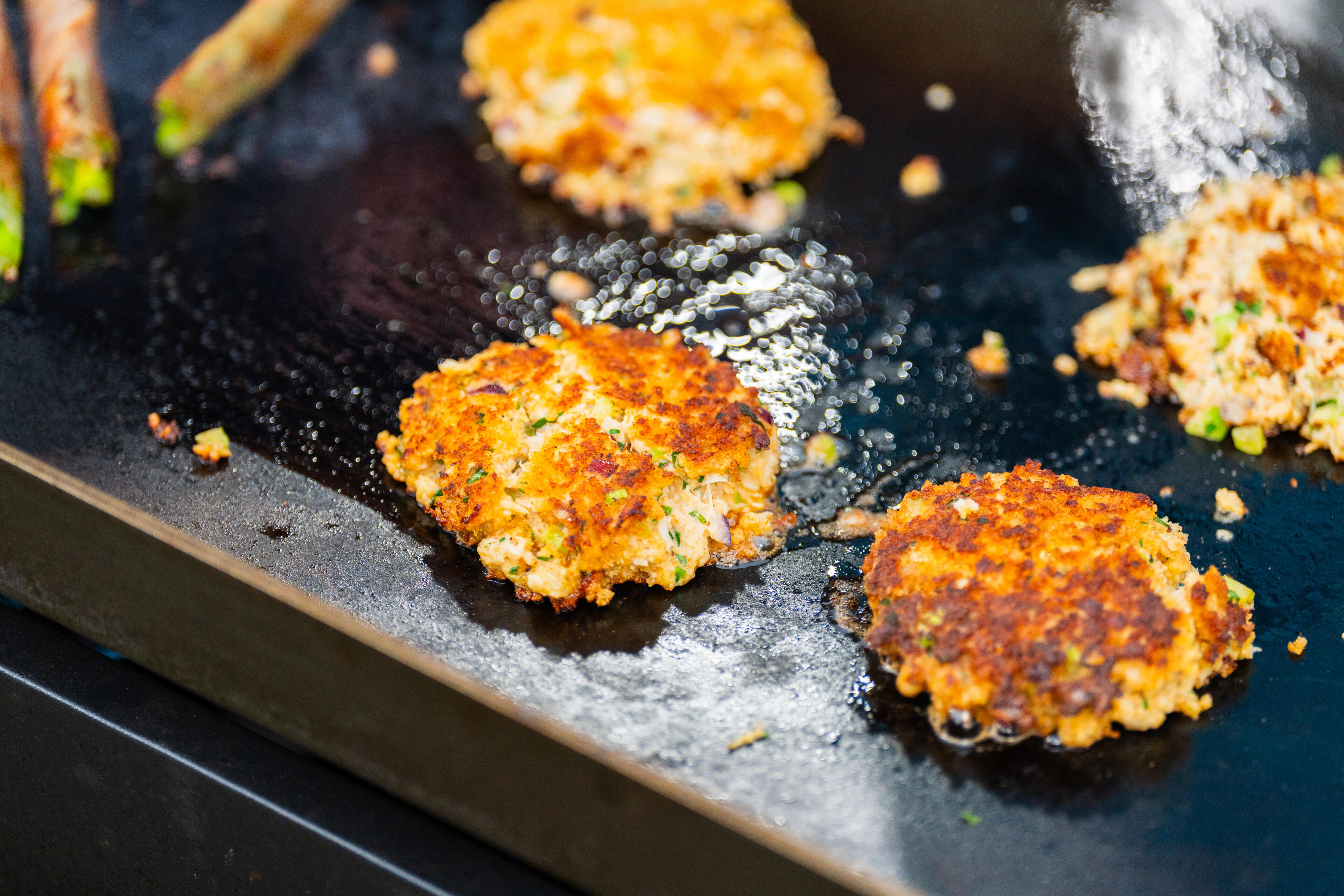 Golden-brown crab cakes sizzling on a dark griddle with melted butter and seasonings
