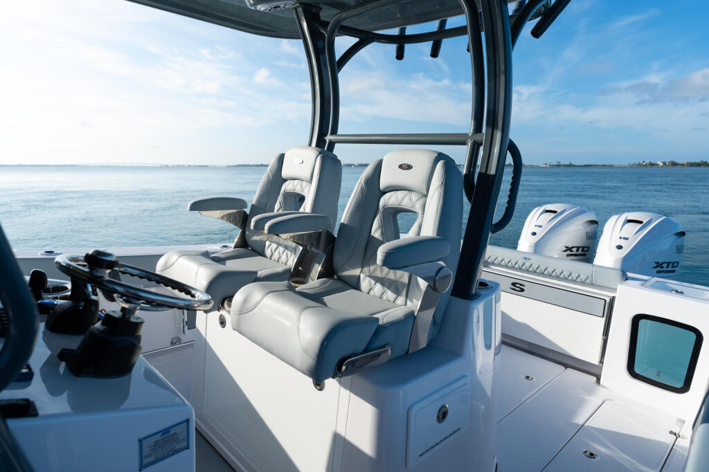 Helm seating and hard-top console of a white center console boat with dual engines on calm blue water