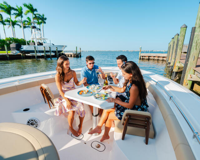Four friends dining and socializing at a table on a boat docked at a marina