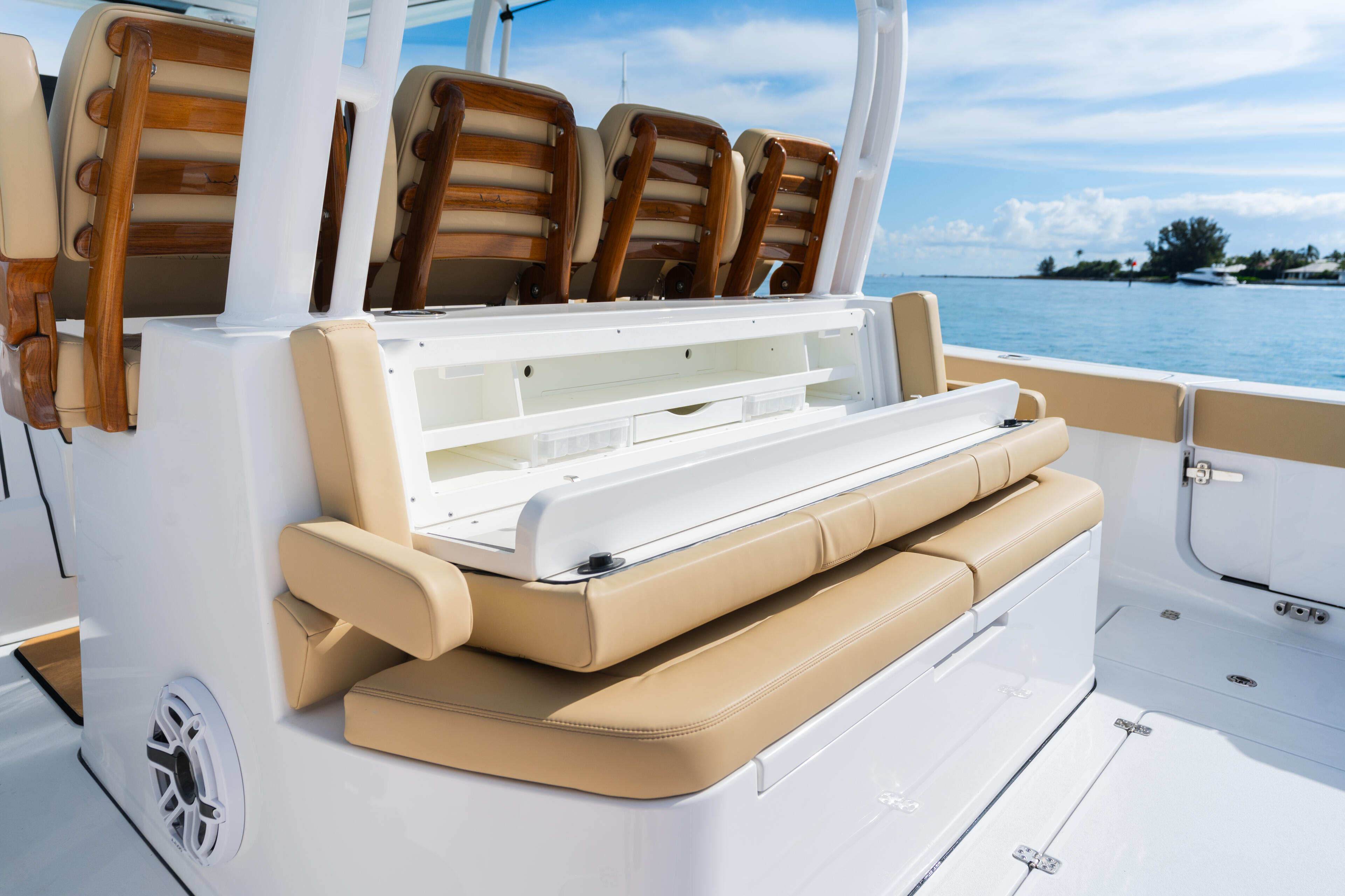Boat's aft seating area with tan cushioned bench seats and wood-trimmed storage above on calm blue water