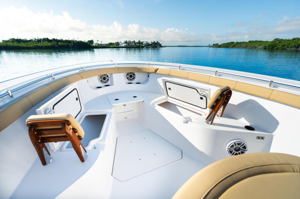 Spacious bow deck with tan seating, storage hatches, and speakers overlooking calm blue water