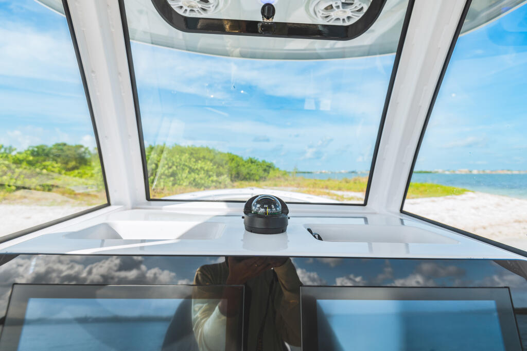 View from inside a center console boat's hard-top with compass and windshield overlooking a sandy beach and calm waters