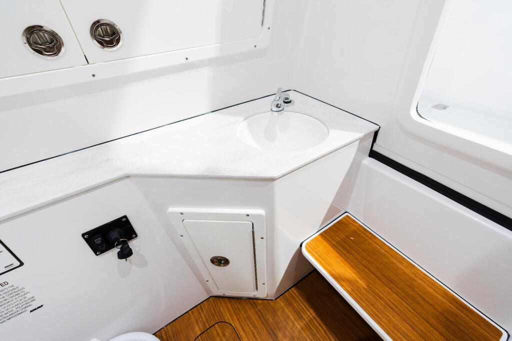 Compact boat cabin bathroom with white fixtures, teak flooring, and ventilation ports