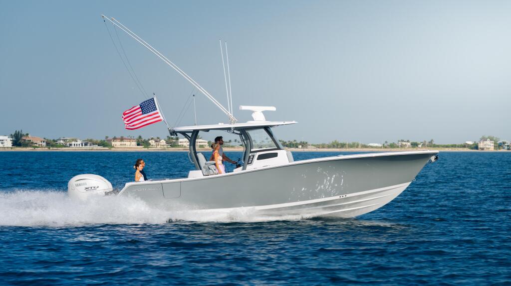 White center console boat running at speed with couple aboard, American flag flying, coastal homes visible along shoreline