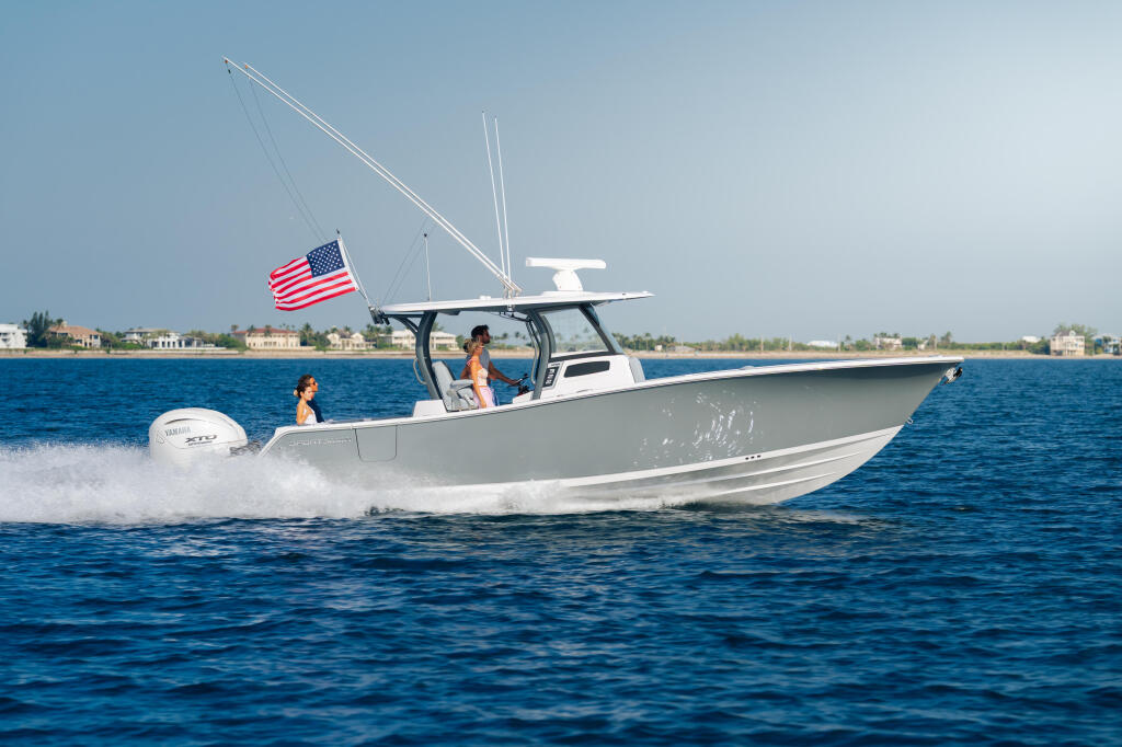 White center console boat running at speed with couple aboard, American flag flying, coastal homes visible along shoreline