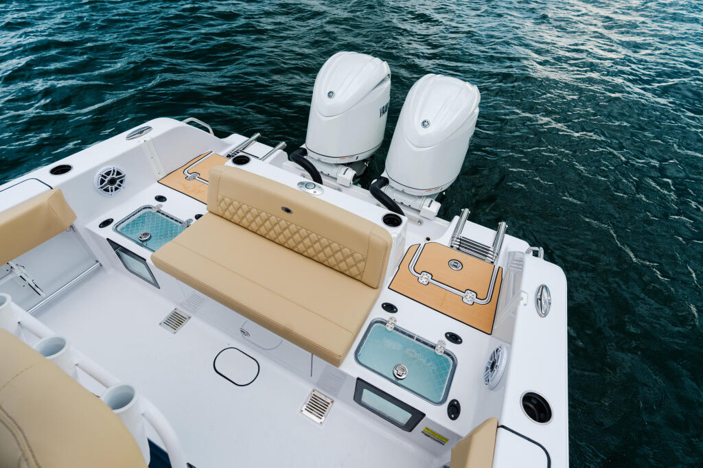 Overhead view of center console boat showing tan and white seating, dual outboard engines, and helm station on calm blue water