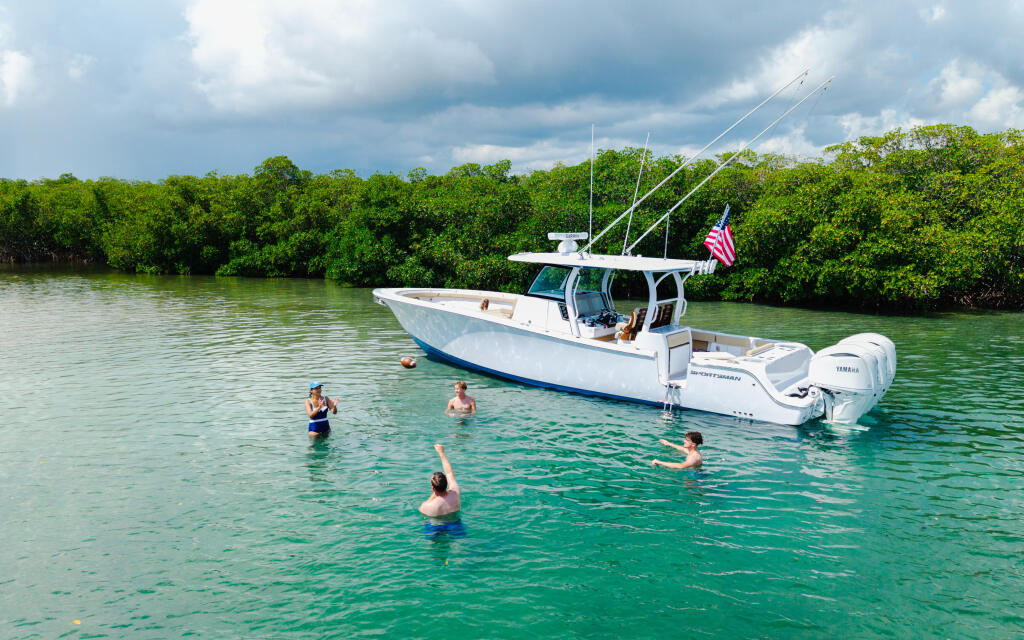 Family swimming and relaxing in turquoise water near a white fishing boat anchored at a sandbar with mangroves in background