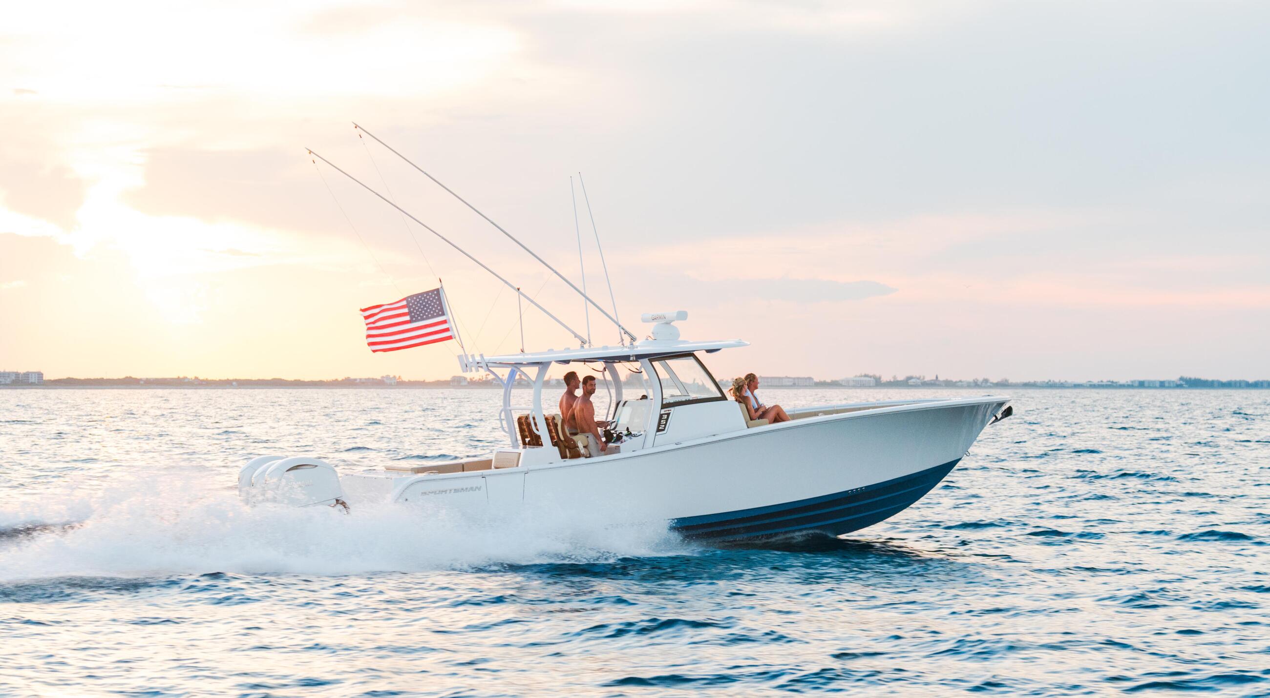 White sportfishing boat with American flag cruising through shallow water at sunset with passengers aboard