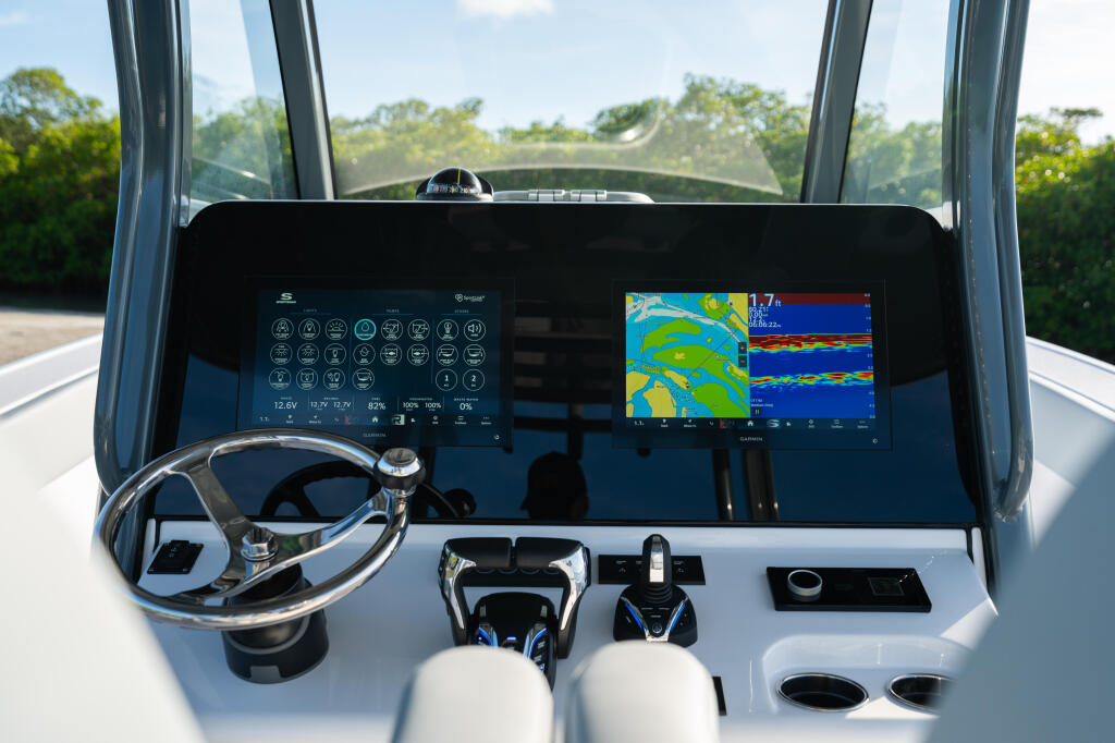Modern boat helm with dual touchscreen displays showing navigation and sonar data, steering wheel, and control panels
