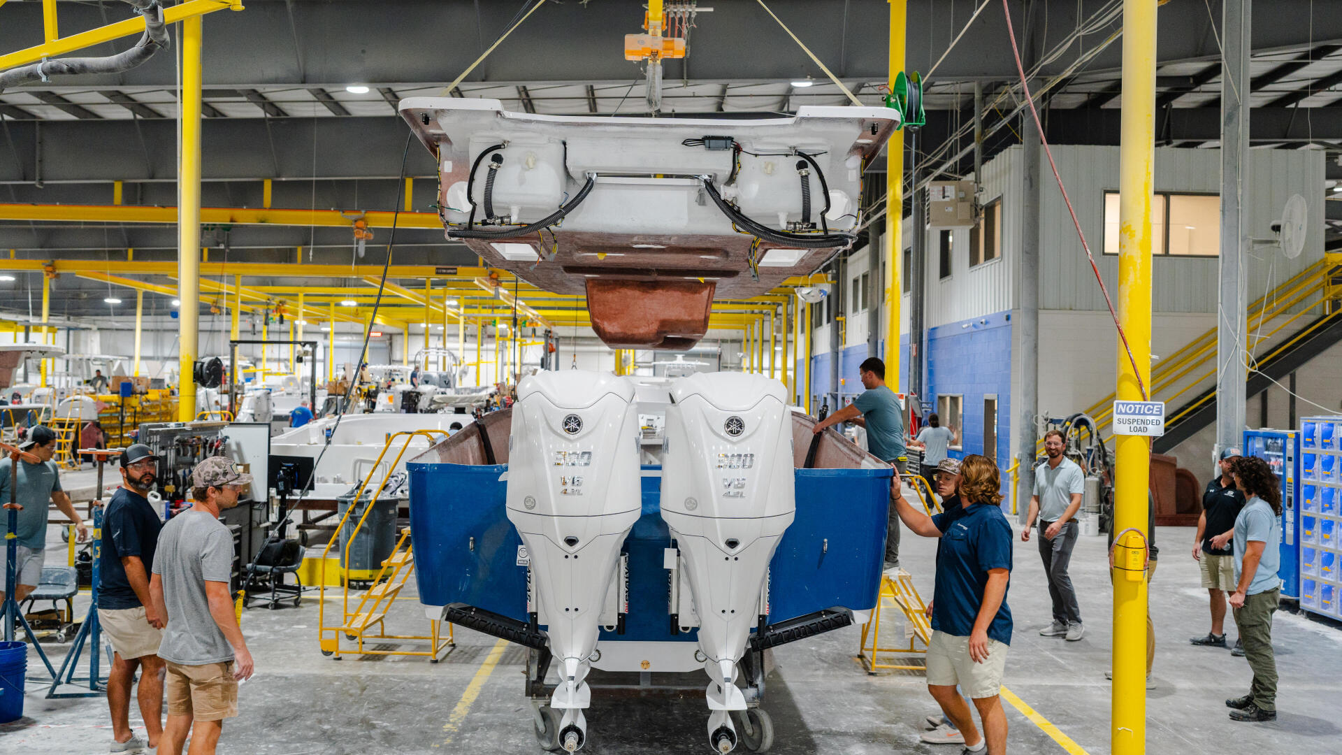 Dual outboard engines being lowered onto a boat hull during manufacturing in a factory facility