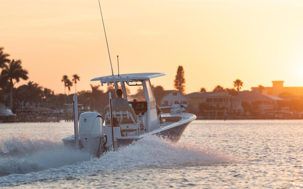 Center console boat running through shallow water at sunset with palm trees and waterfront buildings in the background
