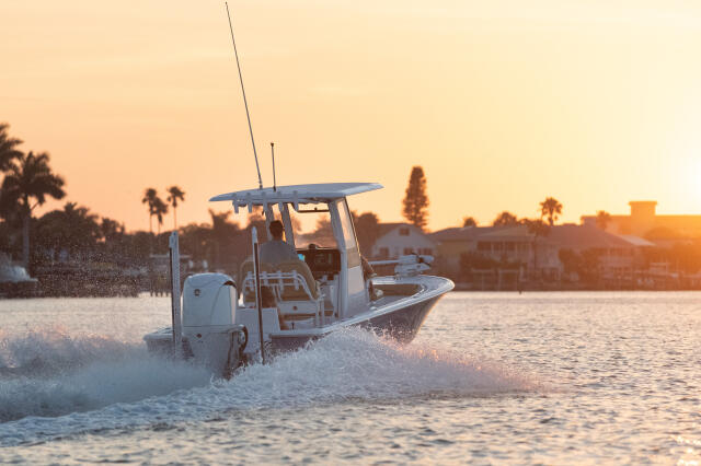 Center console boat running through shallow water at sunset with palm trees and waterfront buildings in the background