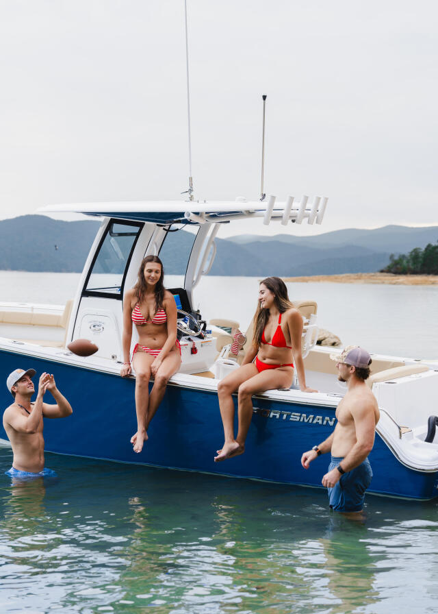 Group relaxing on a blue and white boat in clear shallow water with mountains visible across the lake