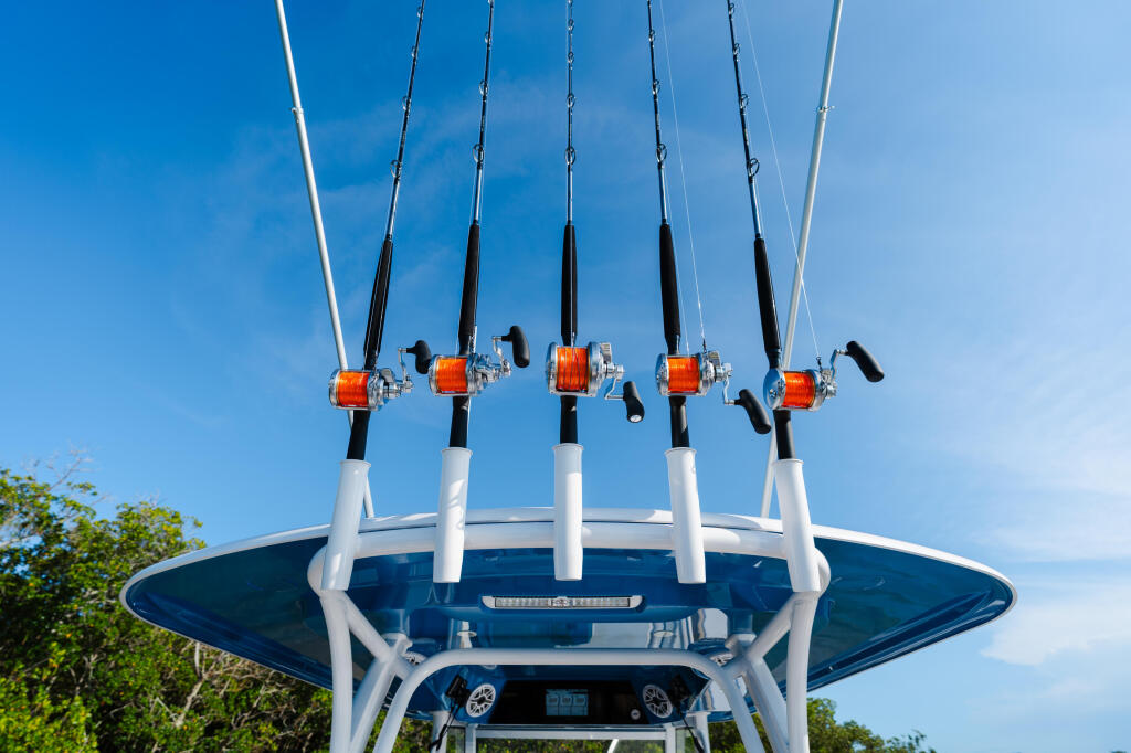 Five fishing rods with orange reels mounted on a white hard-top against clear blue sky