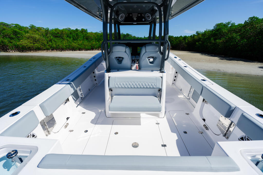 Center console fishing boat with open deck, comfortable seating, and hard-top canopy anchored near a sandy beach with mangroves