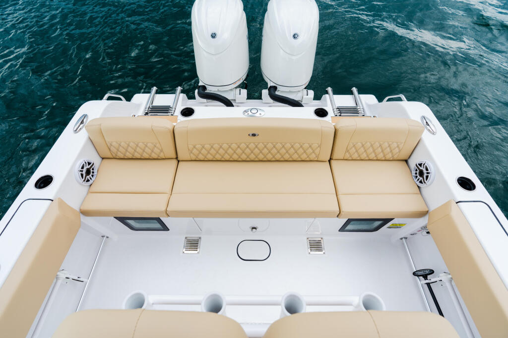 Overhead view of boat's stern seating with tan cushioned lounge, twin white outboard engines, and teal water