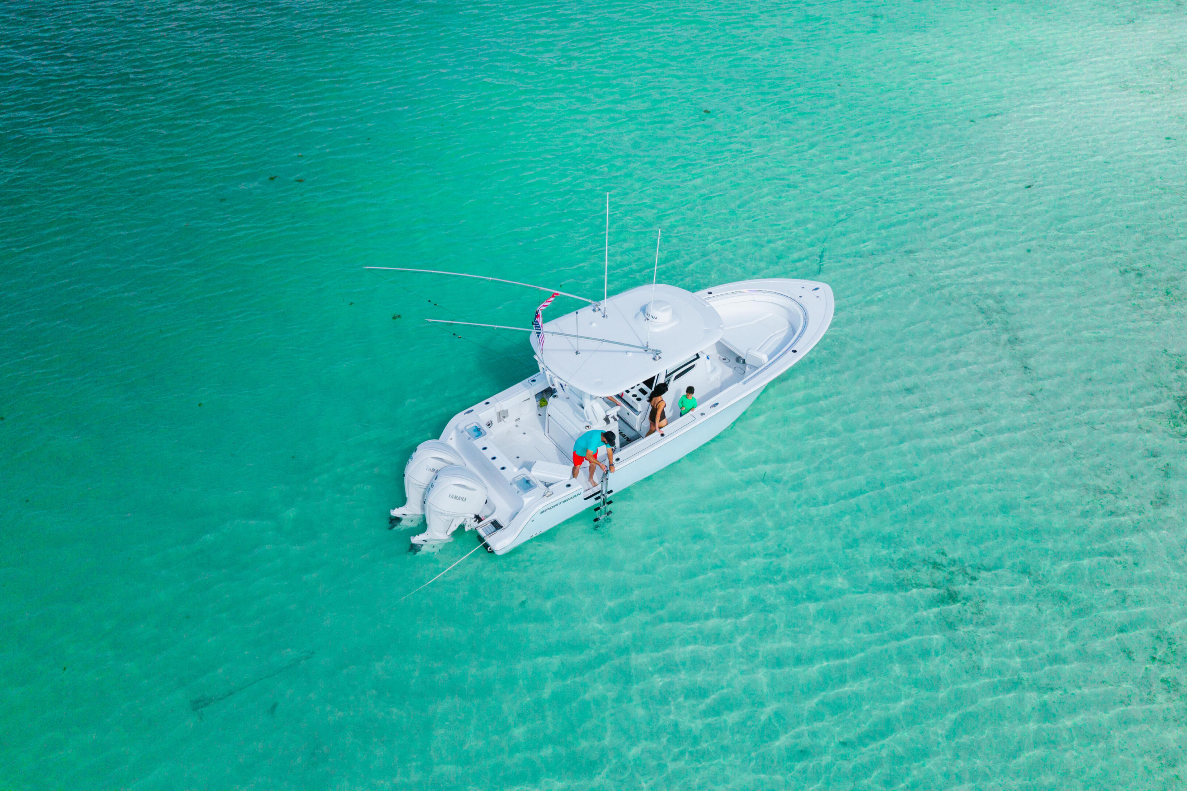 White center console boat anchored in shallow turquoise water with two people aboard