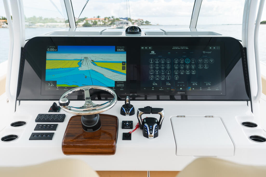 Modern boat helm with dual Garmin chartplotters displaying navigation data and sonar, wooden wheel, and control panels overlooking calm waterway