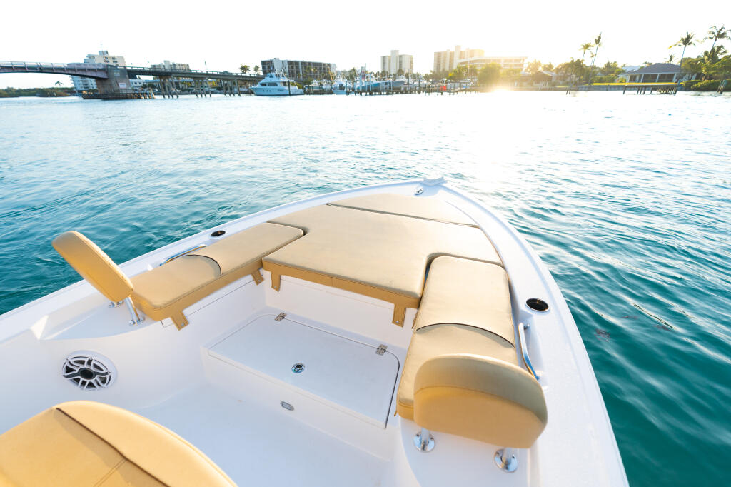 Bow seating with cream cushions and wood accents on a white boat facing a waterfront marina at sunset