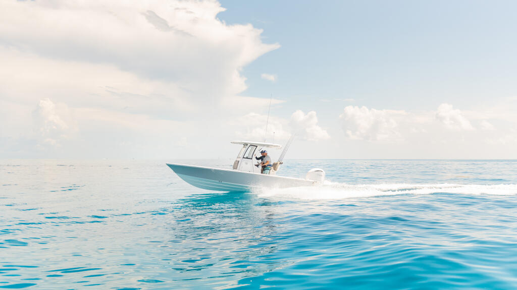 Turquoise and white fishing boat running at speed through calm blue offshore waters under partly cloudy skies