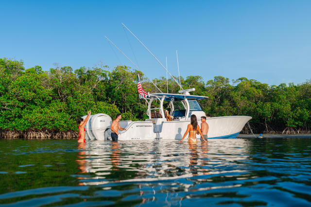 Family swimming and wading around a moored sportsman boat near mangroves