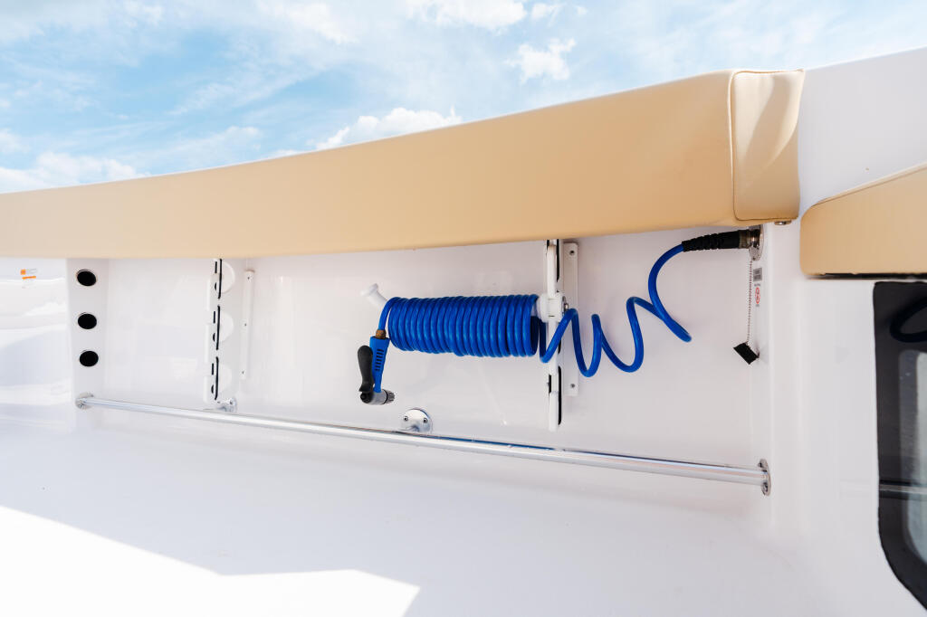 Boat gunwale detail showing blue coiled hose, equipment storage compartments, and tan canvas trim against white hull