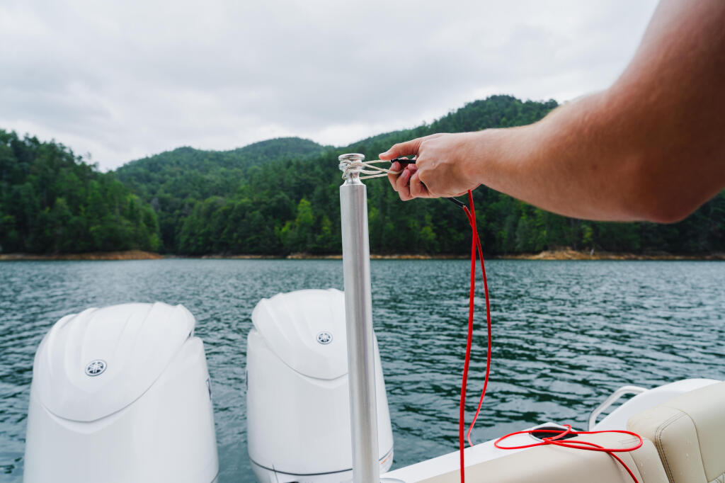 Hand holding a boat's anchor line with forested mountains and calm lake water in background