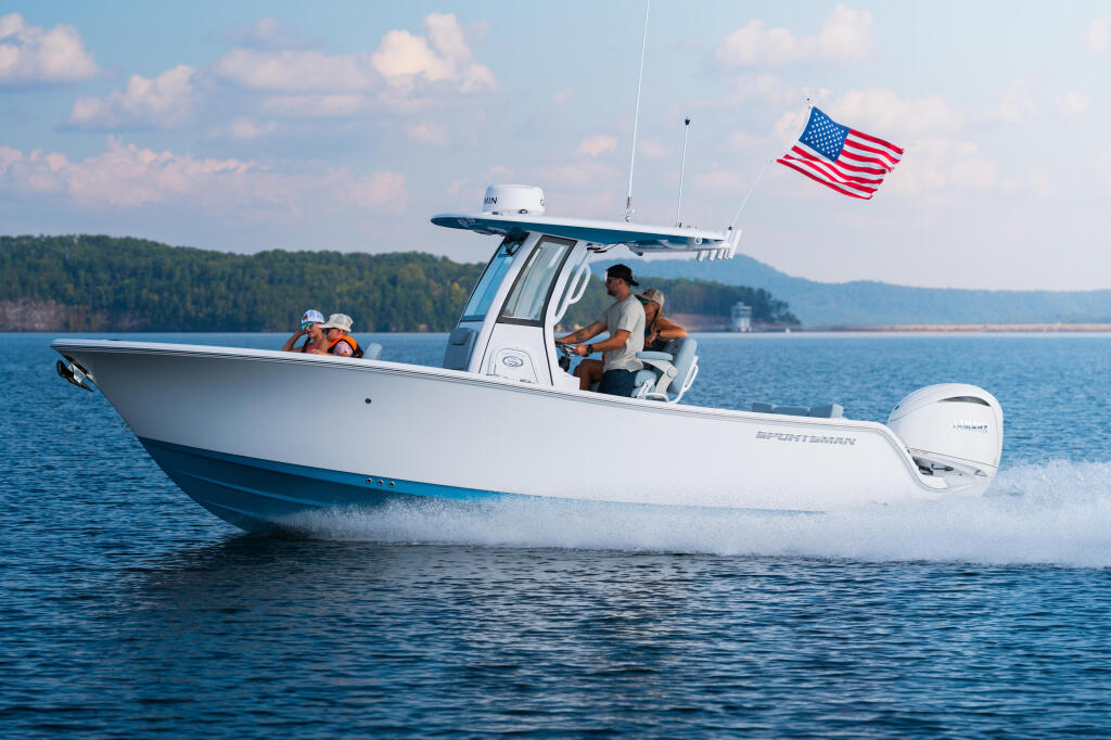White center console boat with hard-top running at speed, two people aboard, American flag flying, forested shoreline in background
