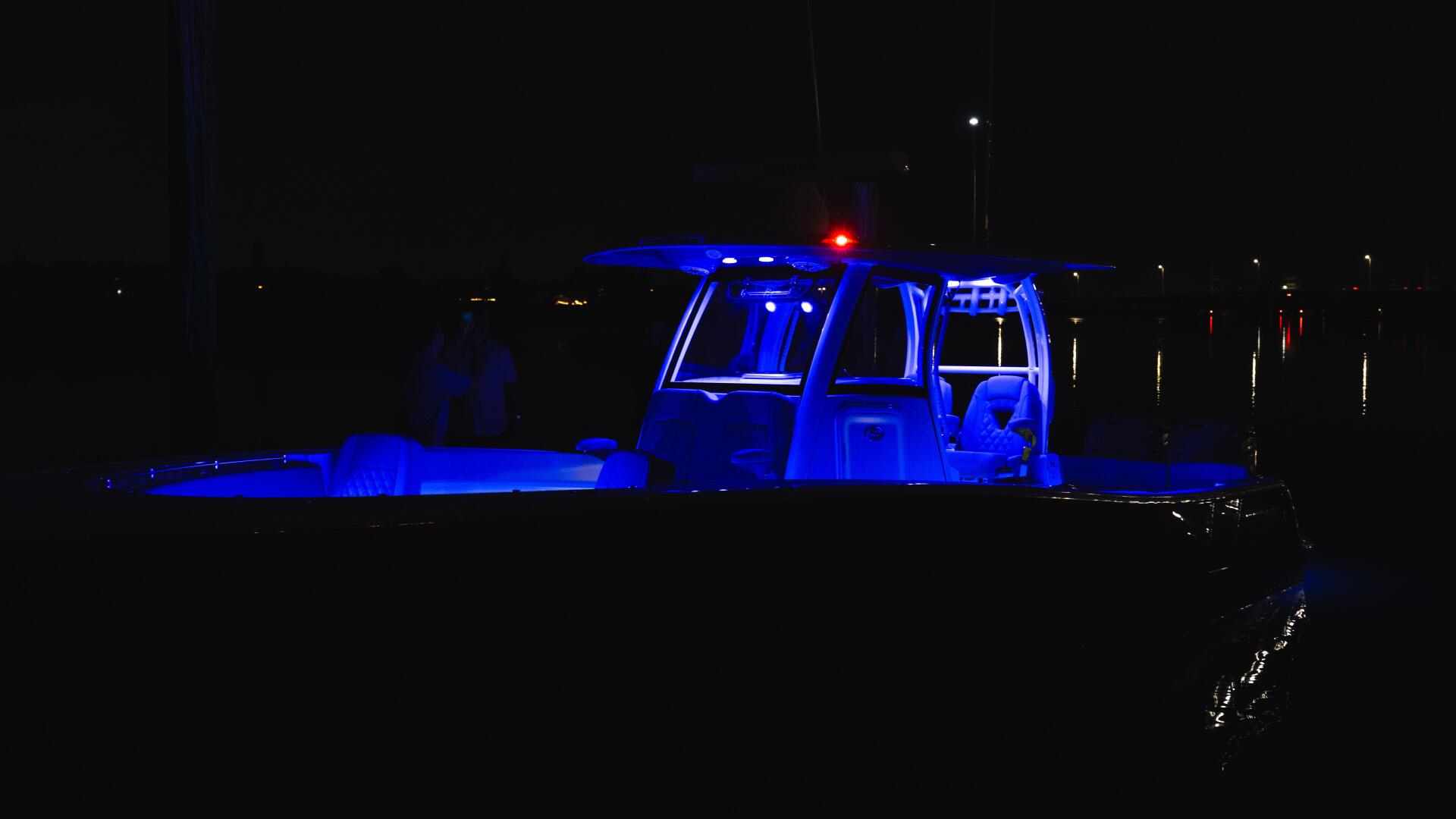 Fishing boat illuminated with blue LED lighting at night, docked at a marina with red beacon light
