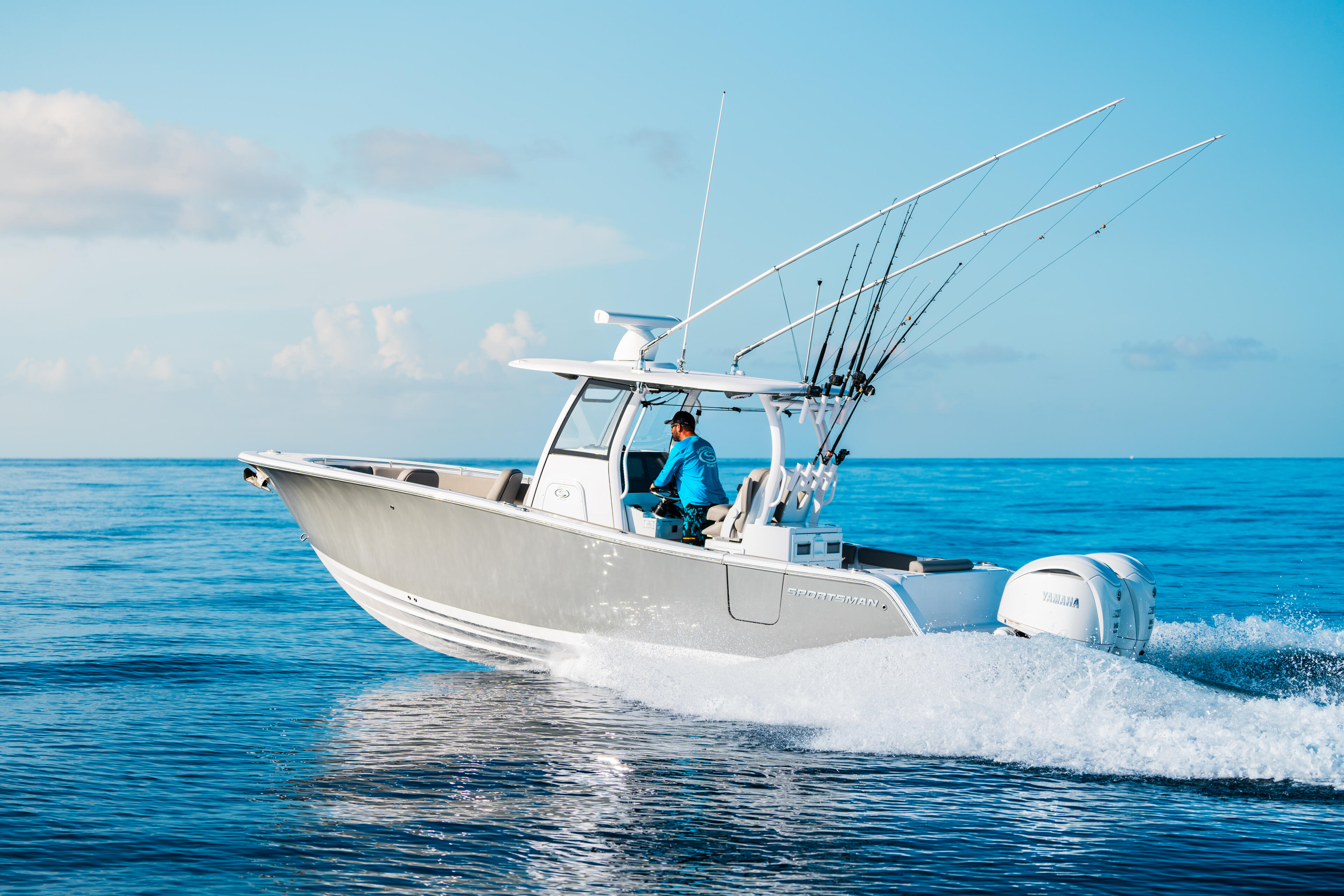 White fishing boat with multiple rod holders running through ocean waves near shore