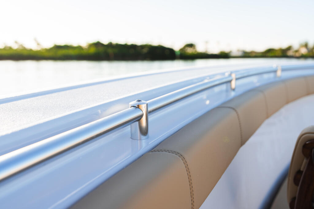 Stainless steel railing and tan seating along boat gunwale with calm water and mangrove shoreline beyond